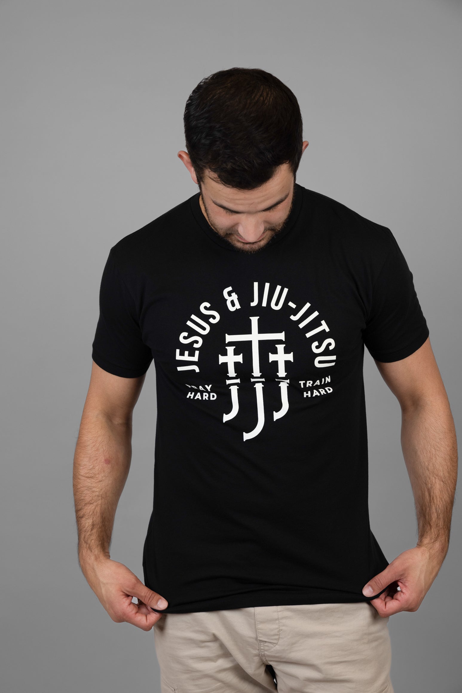 Man wearing a black t-shirt with white "JESUS & JIU-JITSU" text and logo on a gray background
