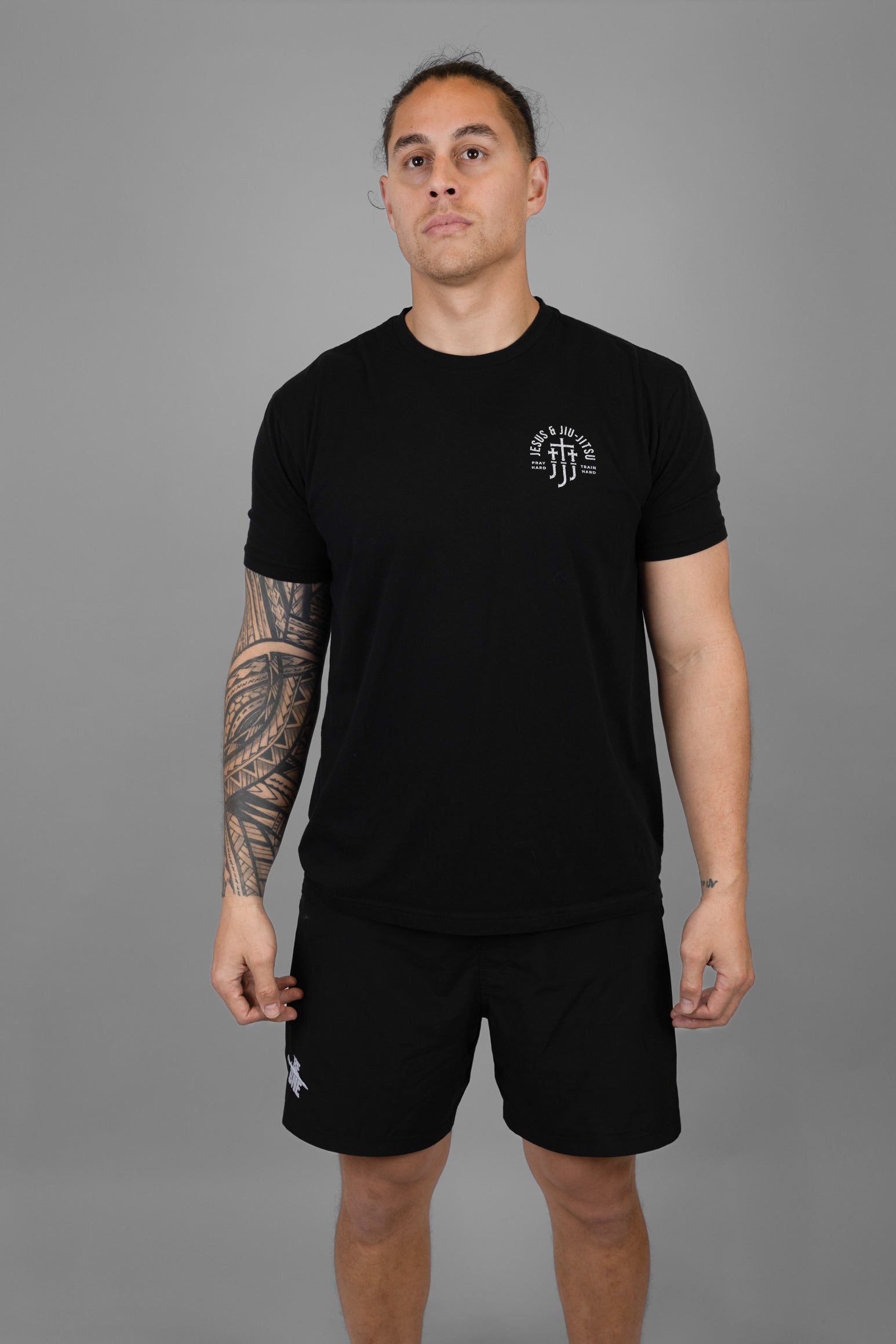 Man wearing a black t-shirt and shorts with a JJJ logo on left chest on a gray background
