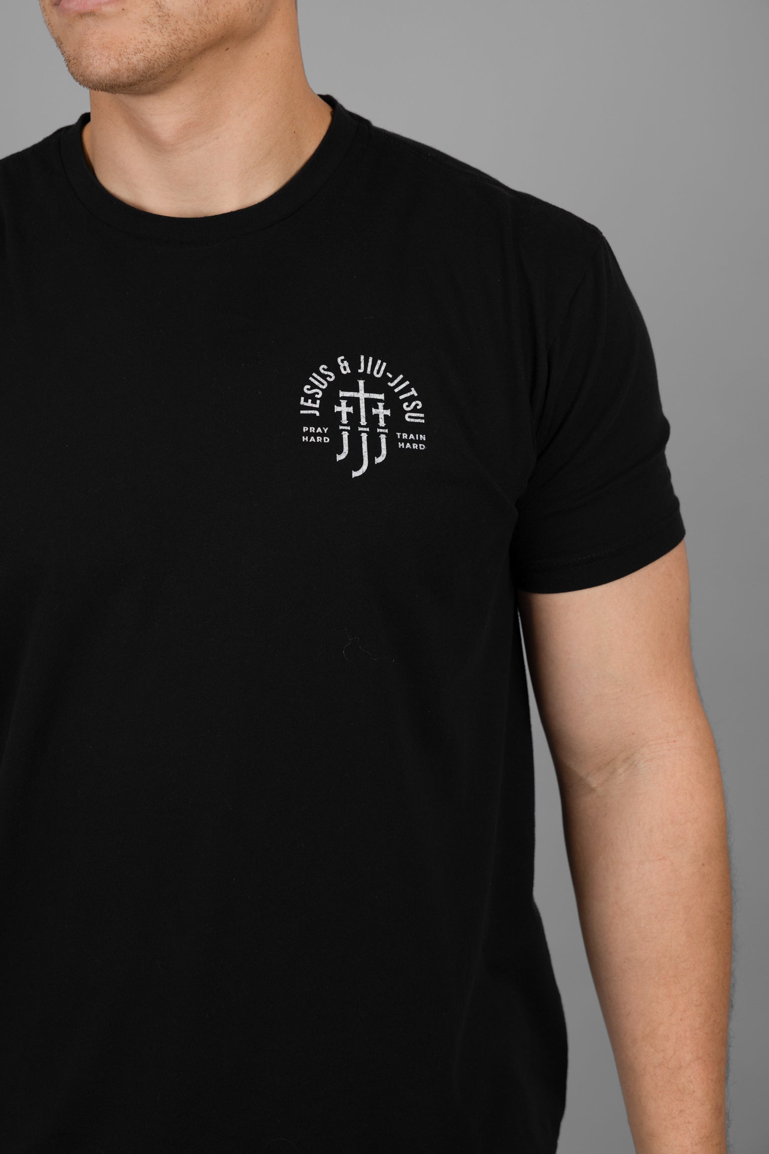 Black t-shirt with a JJJ logo on the chest worn by a person against a gray background
