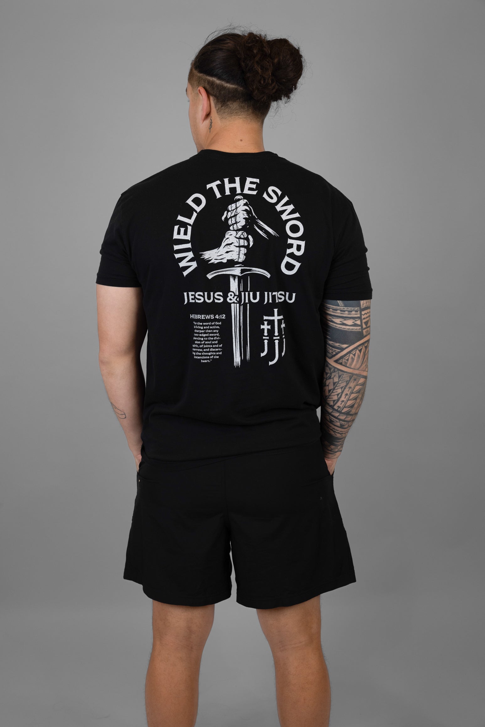 Person wearing a black t-shirt with white text and WIELD THE SWORD graphic on the back, standing against a gray background.