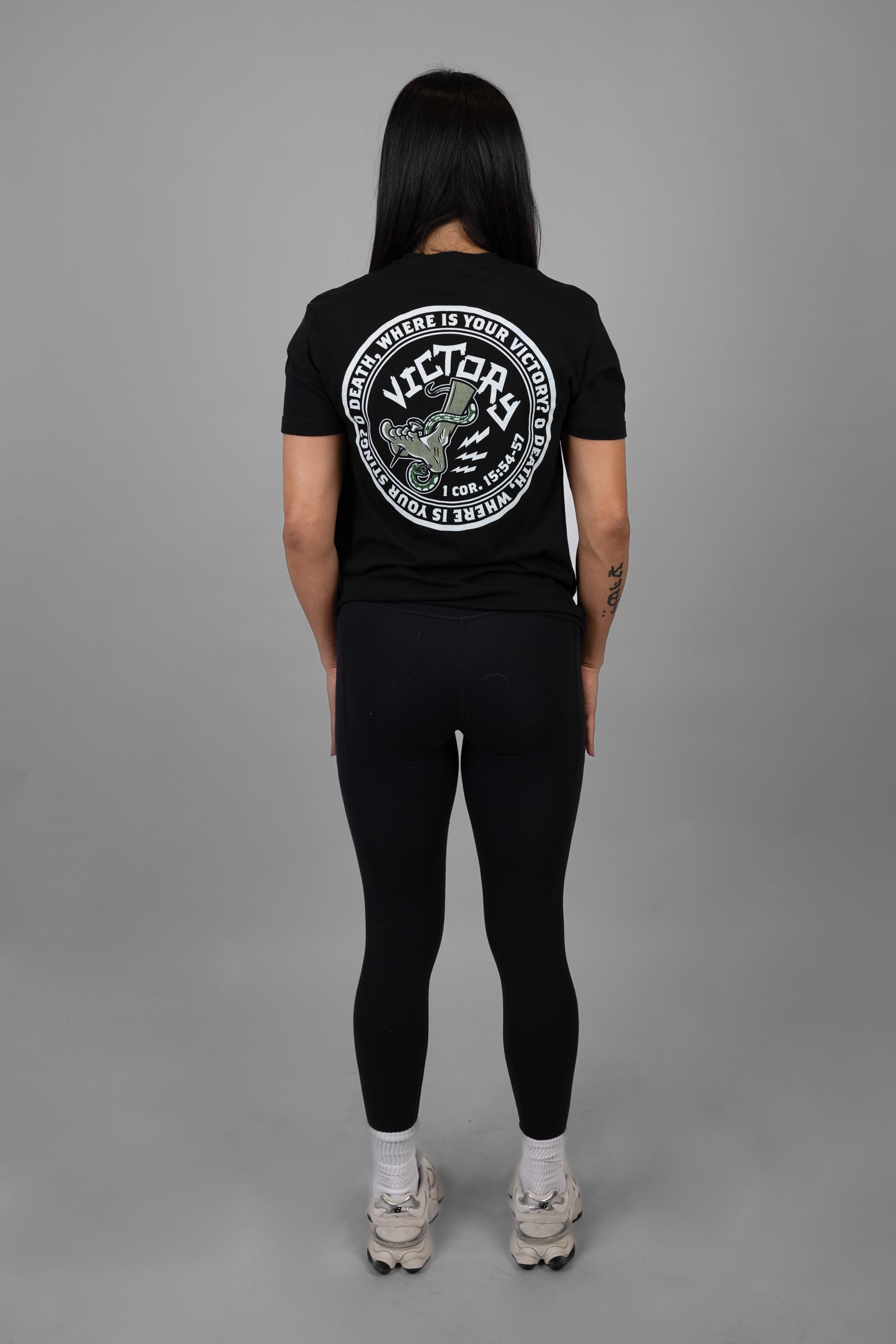 Person wearing a black t-shirt with a VICTORY logo and text on the back, standing against a gray background