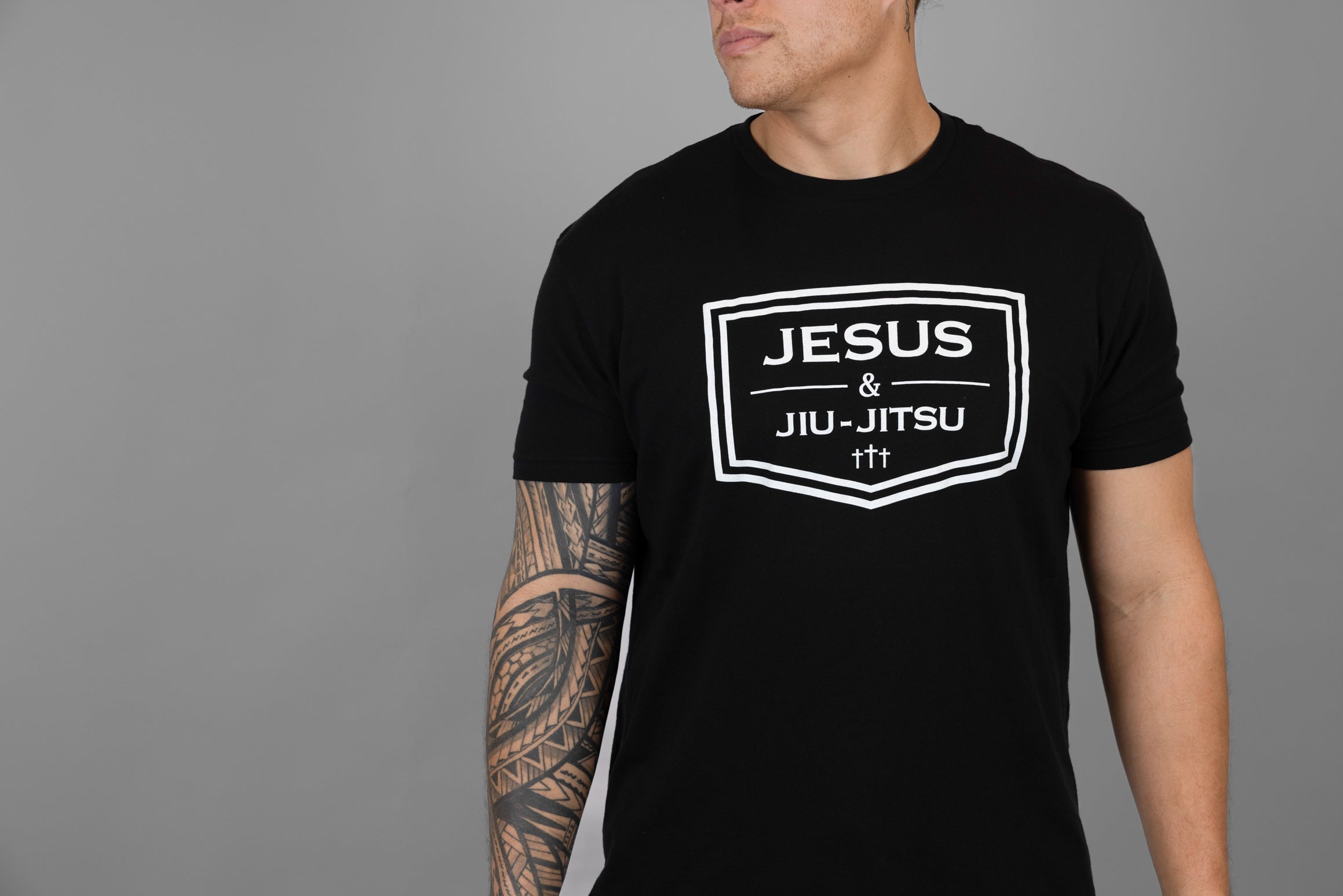 Person wearing a black t-shirt with 'Jesus & Jiu-Jitsu' design on a gray background