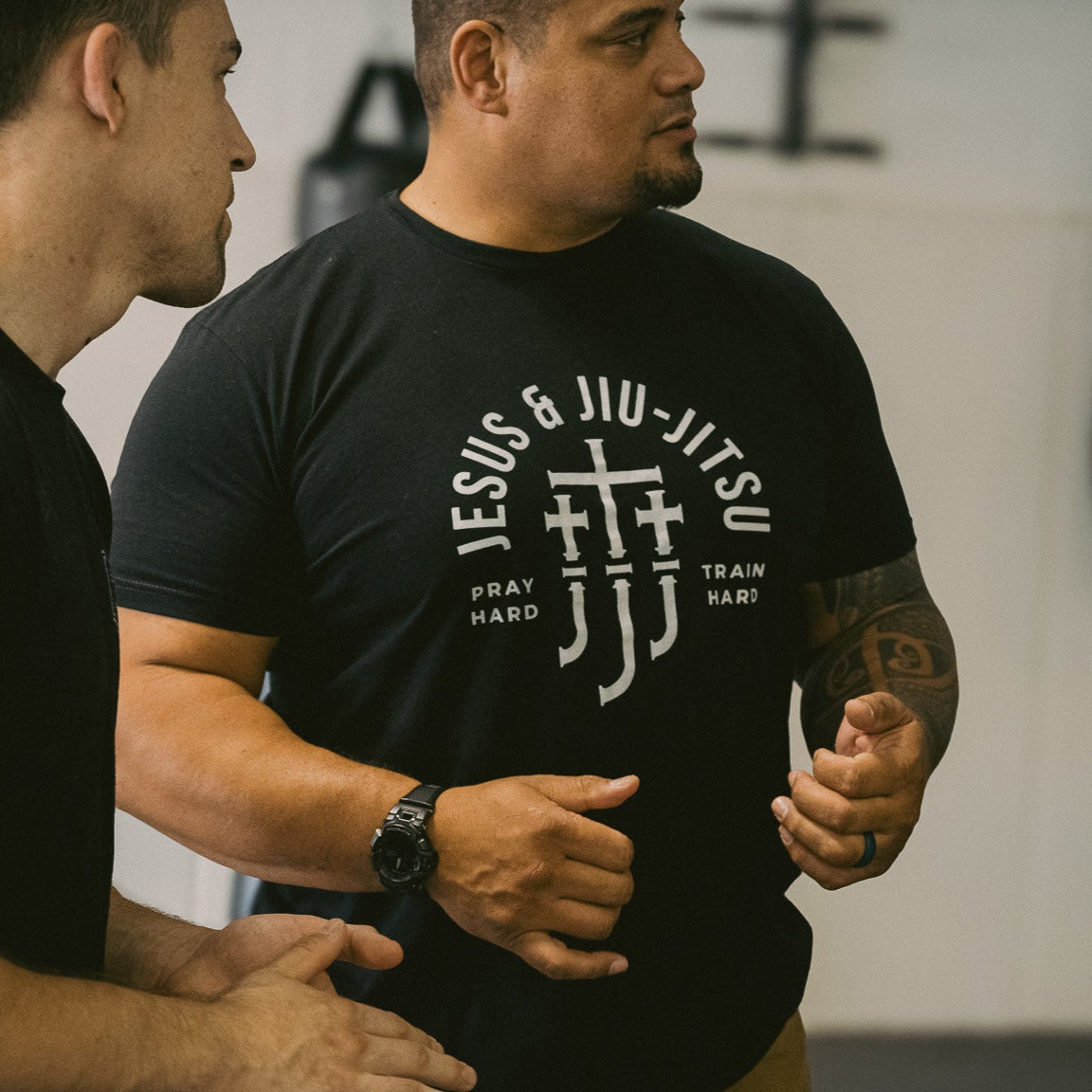 Man wearing a black t-shirt with white "JESUS & JIU-JITSU" text and logo on a gray background