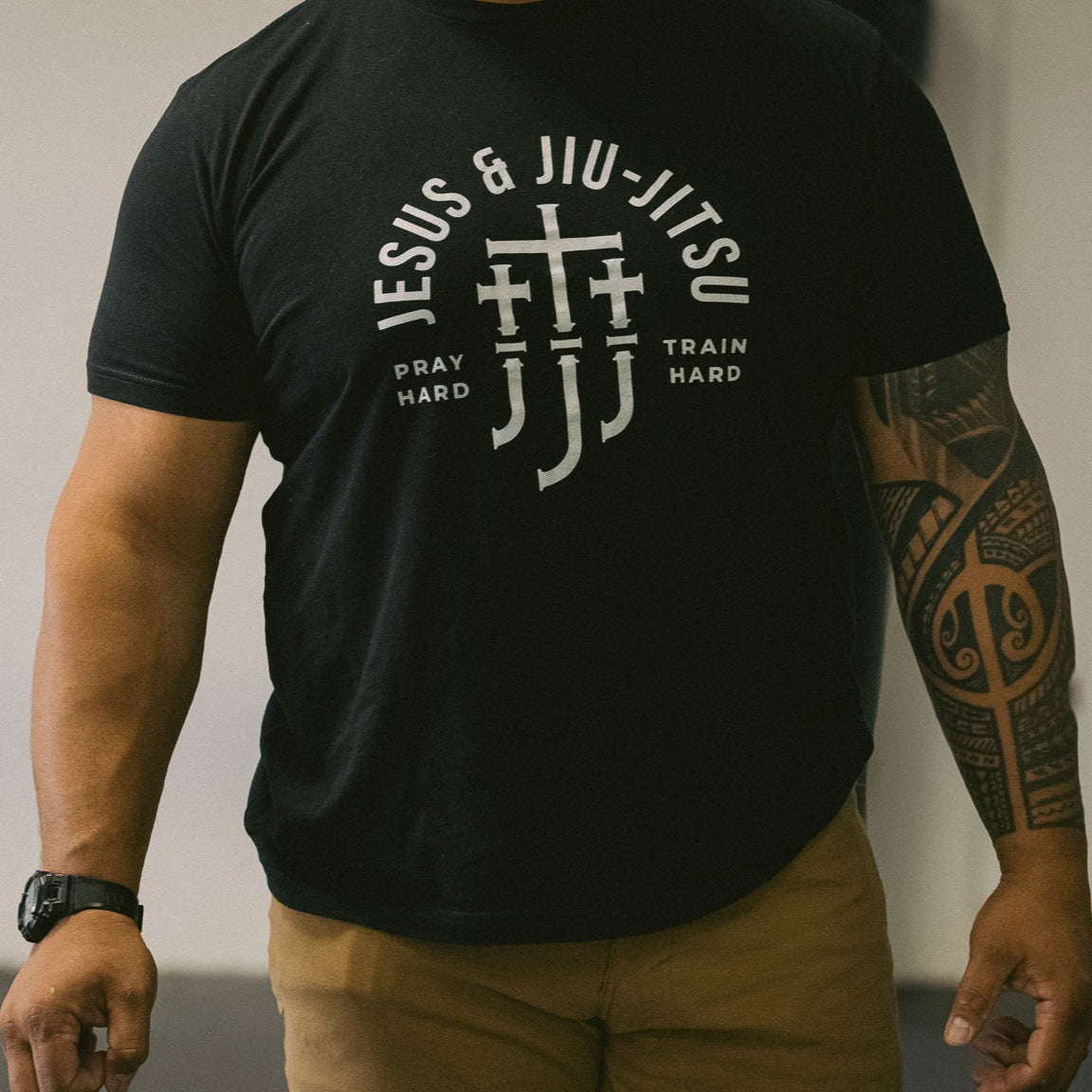 Man wearing a black t-shirt with white "JESUS & JIU-JITSU" text and logo on a gray background