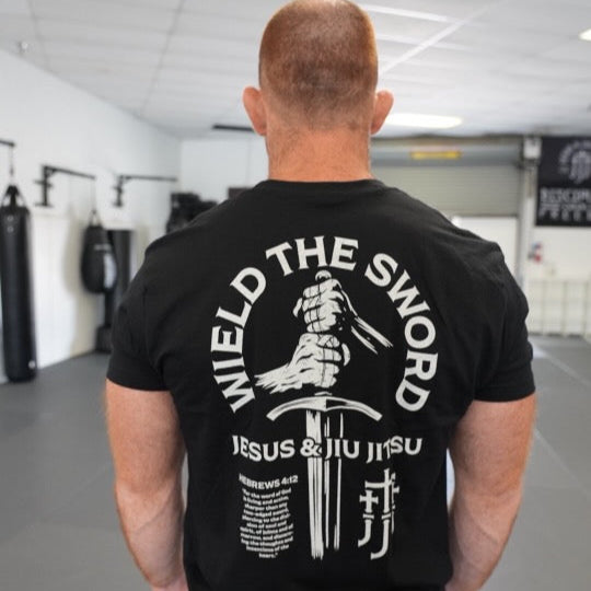 Man wearing a black t-shirt with a WIELD THE SWORD graphic design and text in a gym setting