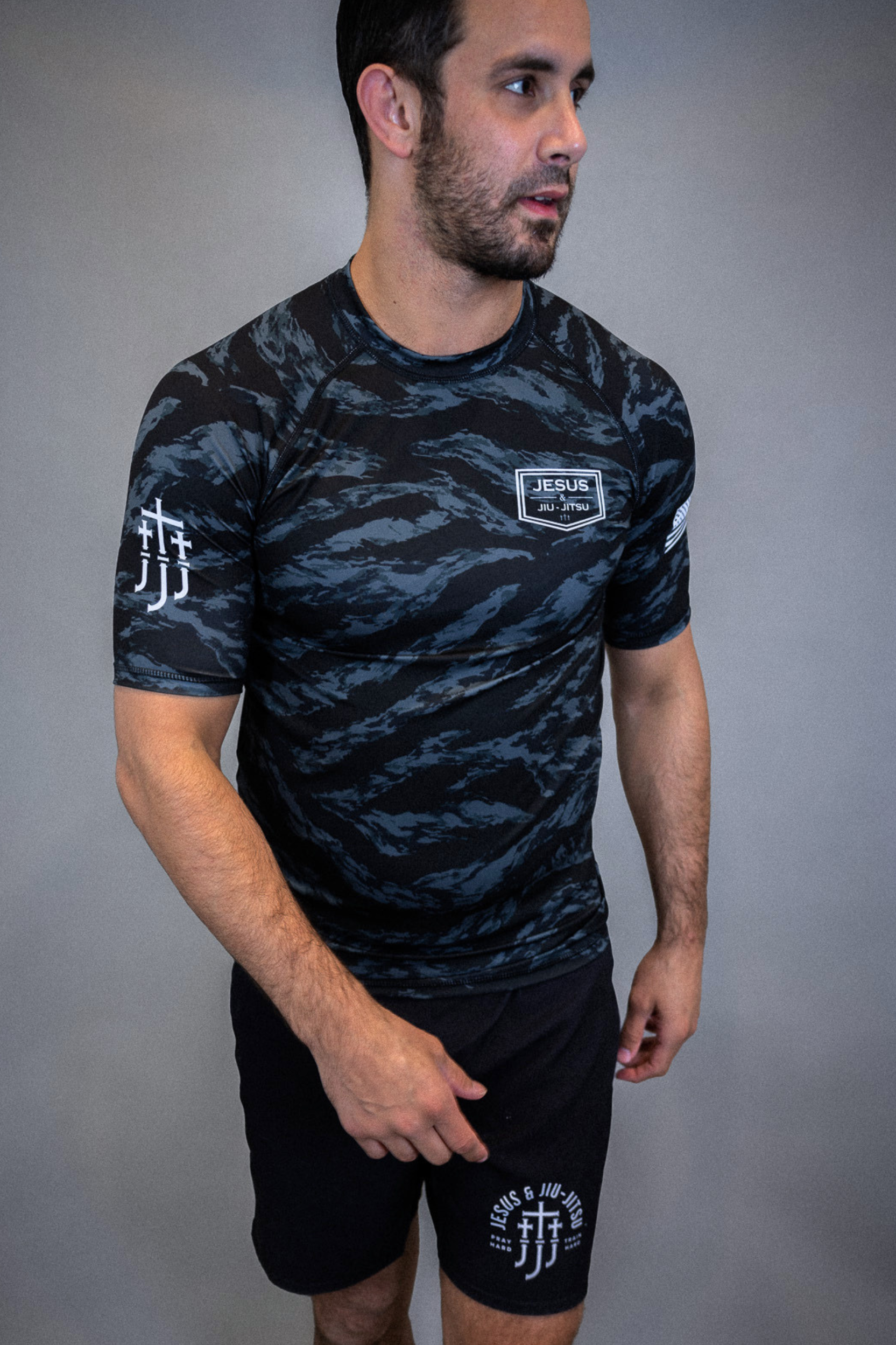 man wearing camo rashguard with Jesus and Jiu Jitsu logo on left chest and JJJ on right sleeve