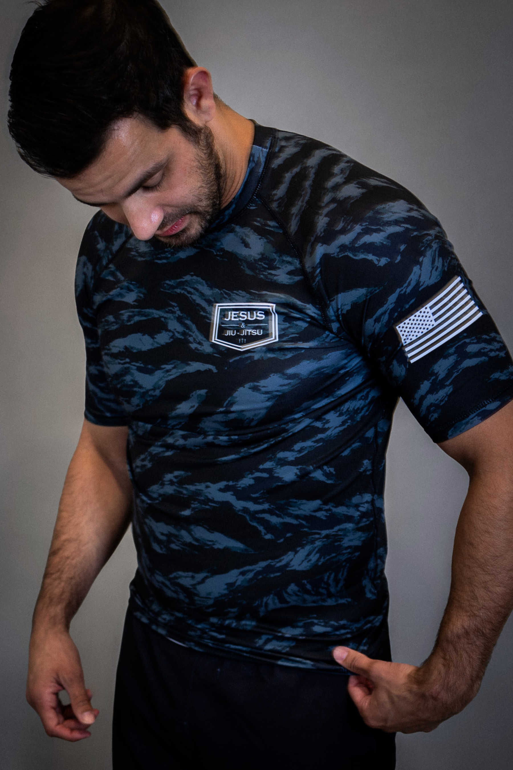 man wearing camo rashguard with Jesus and Jiu Jitsu logo on left chest and flag on left sleeve