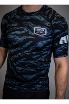 man wearing camo rashguard with Jesus and Jiu Jitsu logo on left chest and flag on left sleeve