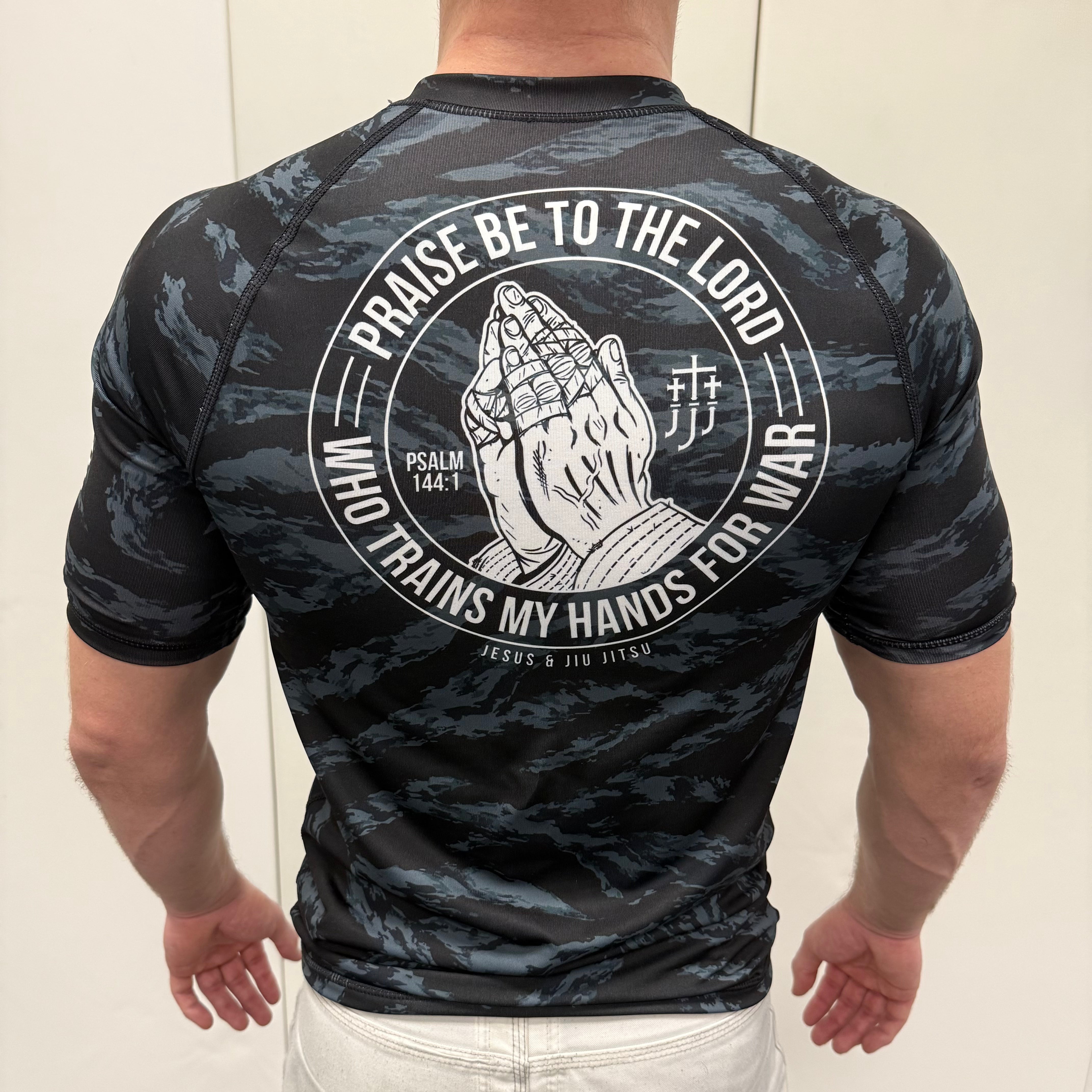 Man wearing black tiger camo rashguard with prayer hands graphic on back