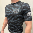 Man wearing black tiger camo rashguard with JJJ logo on left chest and American flag on right shoulder