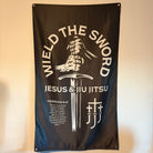 Black flag with hands holding sword graphic with text "WIELD THE SWORD JESUS & JIU JITSU"