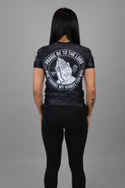 Woman wearing black tiger camo rashguard with prayer hands graphic on back and American flag on left shoulder