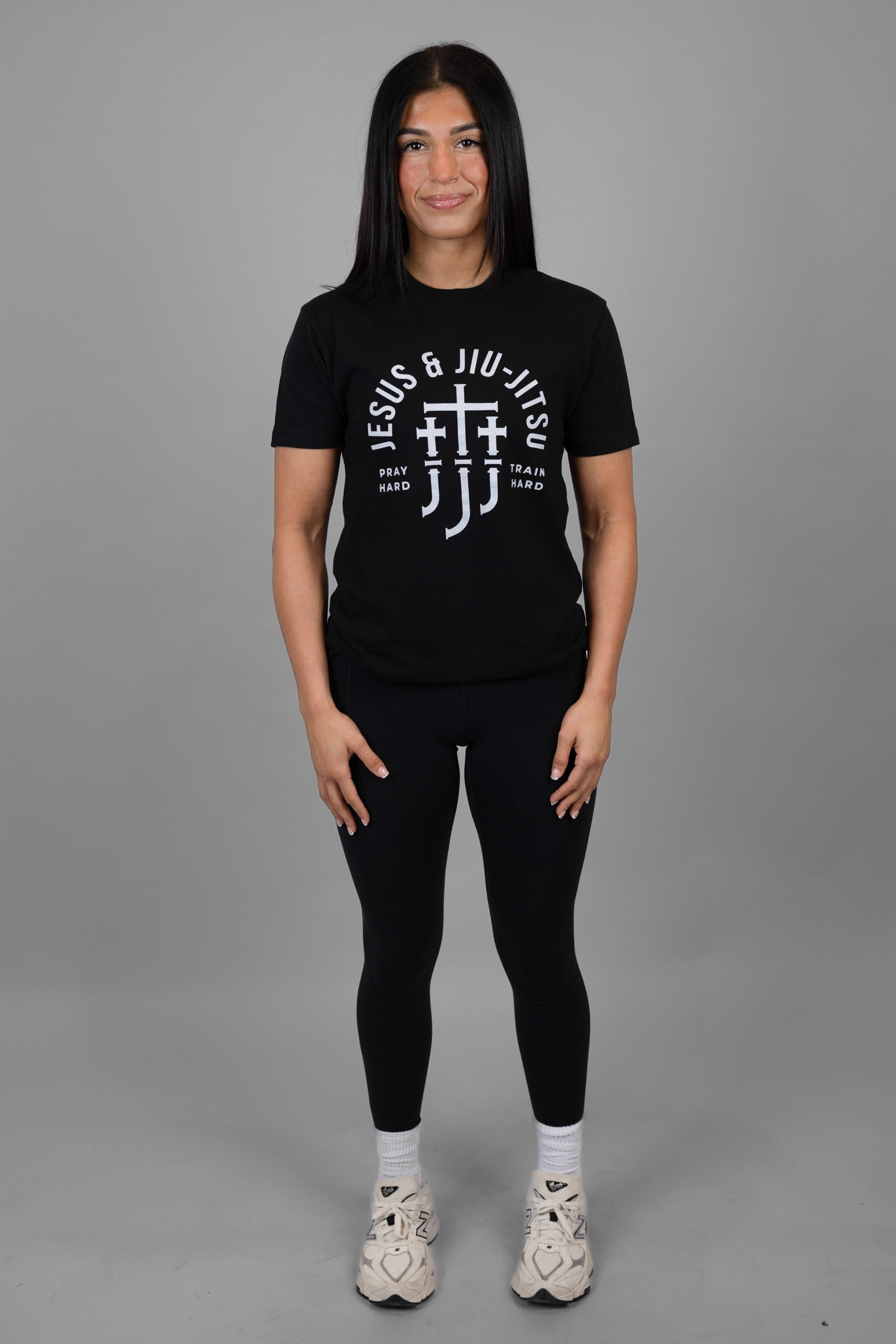 Woman wearing a black t-shirt with white "JESUS & JIU-JITSU" text and logo on a gray background