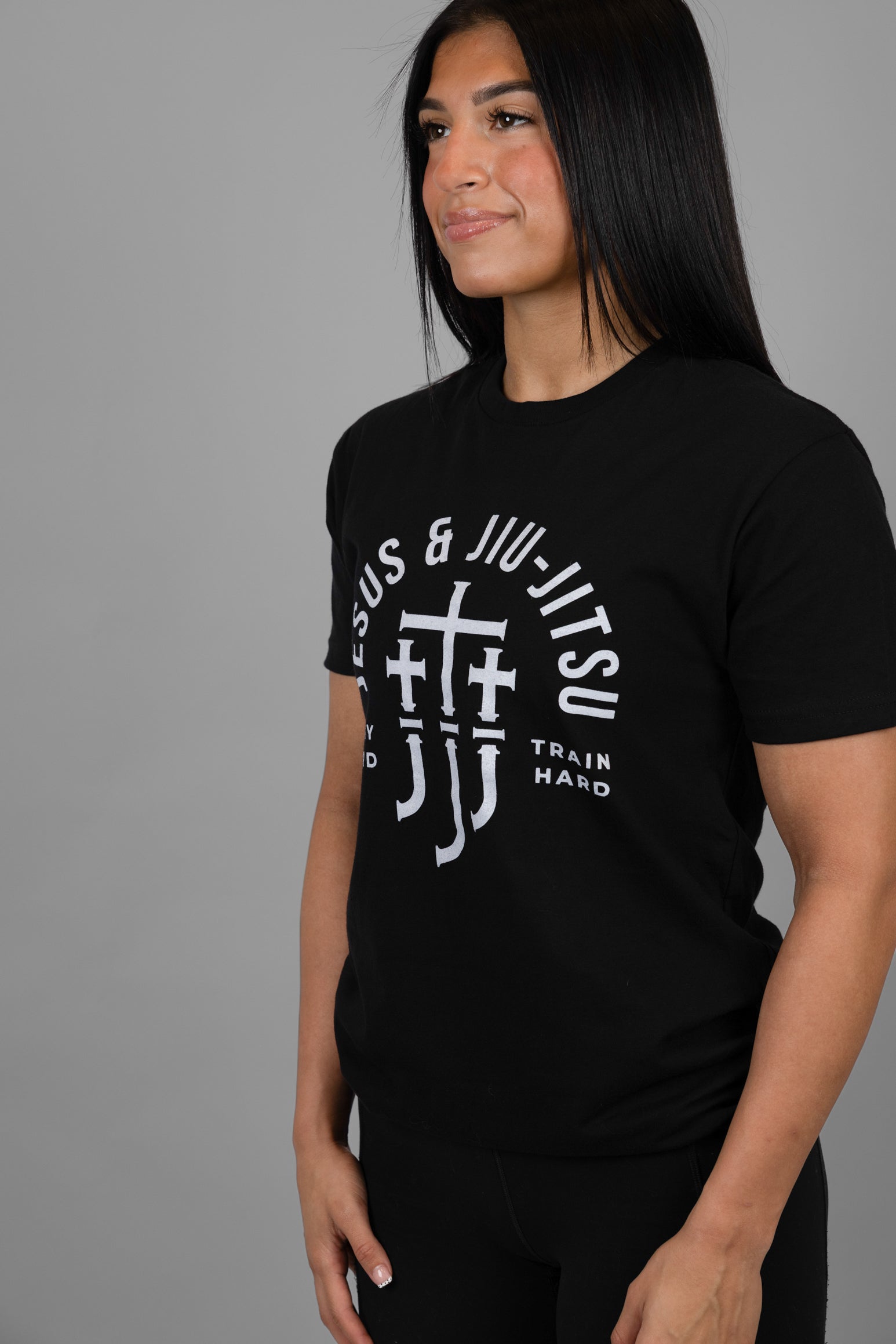 Woman wearing a black t-shirt with white "JESUS & JIU-JITSU" text and logo on a gray background