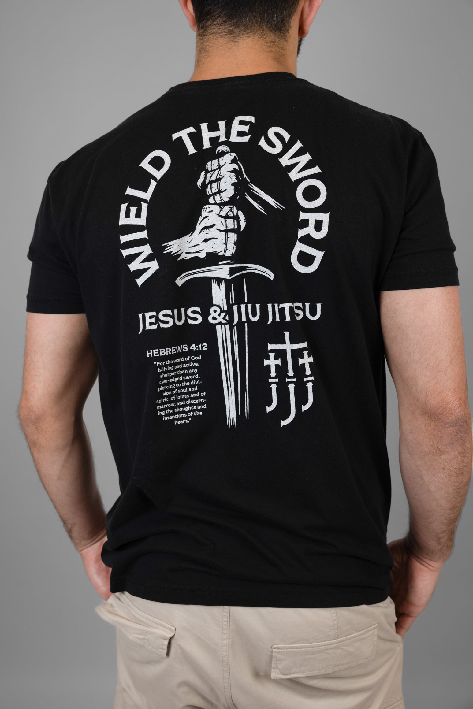 Black t-shirt with white WIELD THE SWORD graphic and text on the back, worn by a person against a gray background
