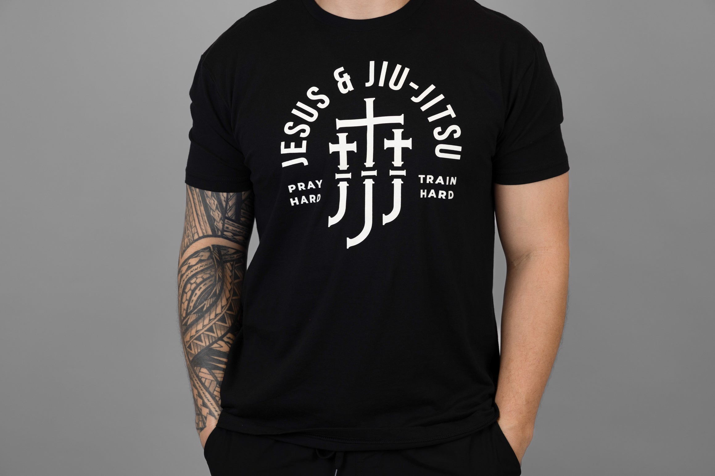 Man wearing a black t-shirt with white "JESUS & JIU-JITSU" text and logo on a gray background