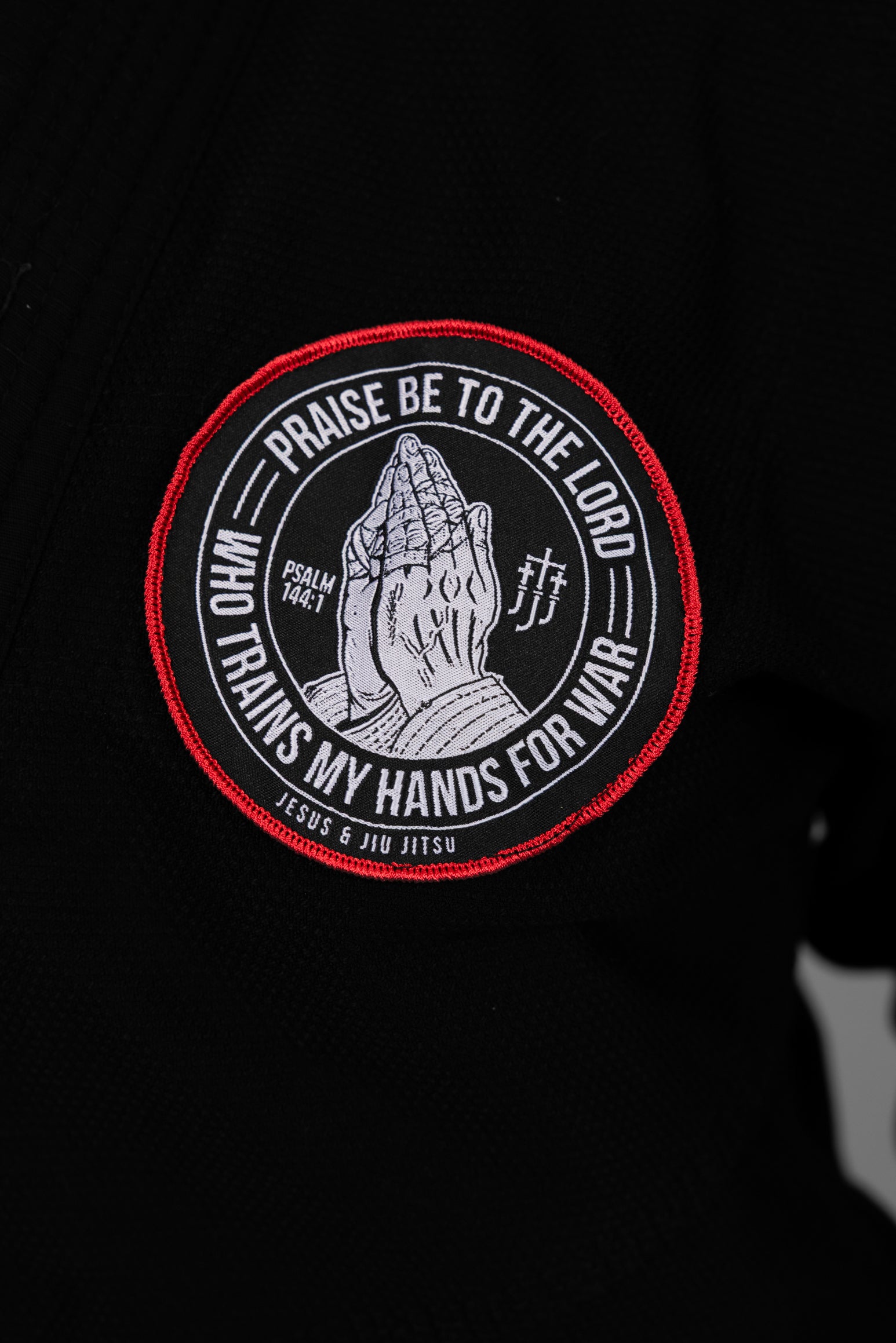 Patch with praying hands design and "PRAISE BE TO THE LORD WHO TRAINS MY HANDS FOR WAR" text on a black gi