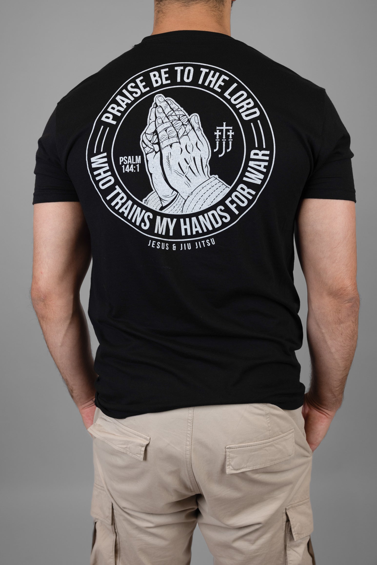 man wearing black tee with praying hands graphic on back with text "PRAISE BE TO THE LORD WHO TRAINS MY HANDS FOR WAR"