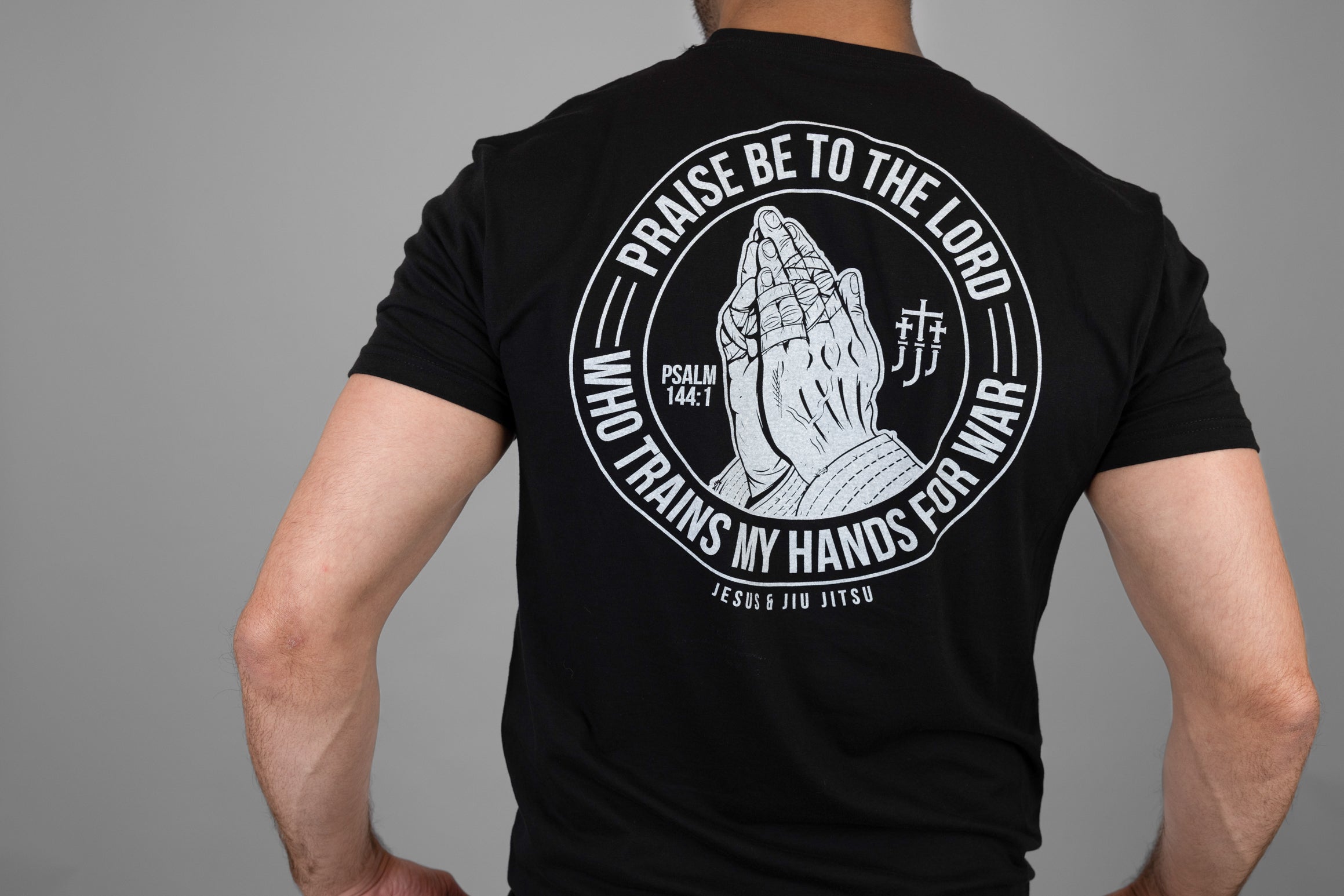 man wearing black tee with praying hands graphic on back with text "PRAISE BE TO THE LORD WHO TRAINS MY HANDS FOR WAR"