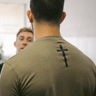 rear view of man wearing green tee with black cross