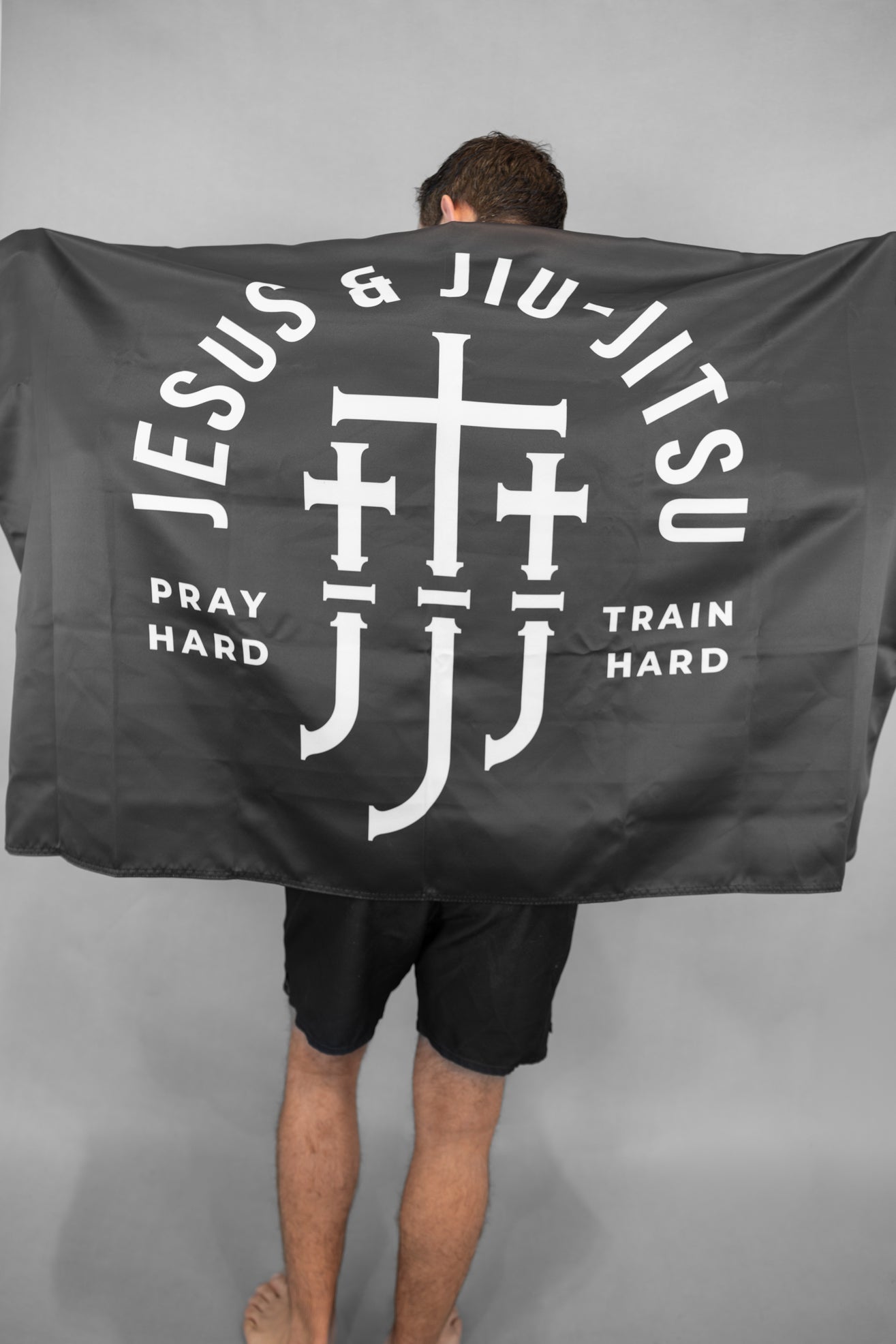 Man holding Black flag with Jesus & Jiu Jitsu logo featuring "PRAY HARD TRAIN HARD" text