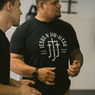 Man wearing a black t-shirt with white "JESUS & JIU-JITSU" text and logo on a gray background