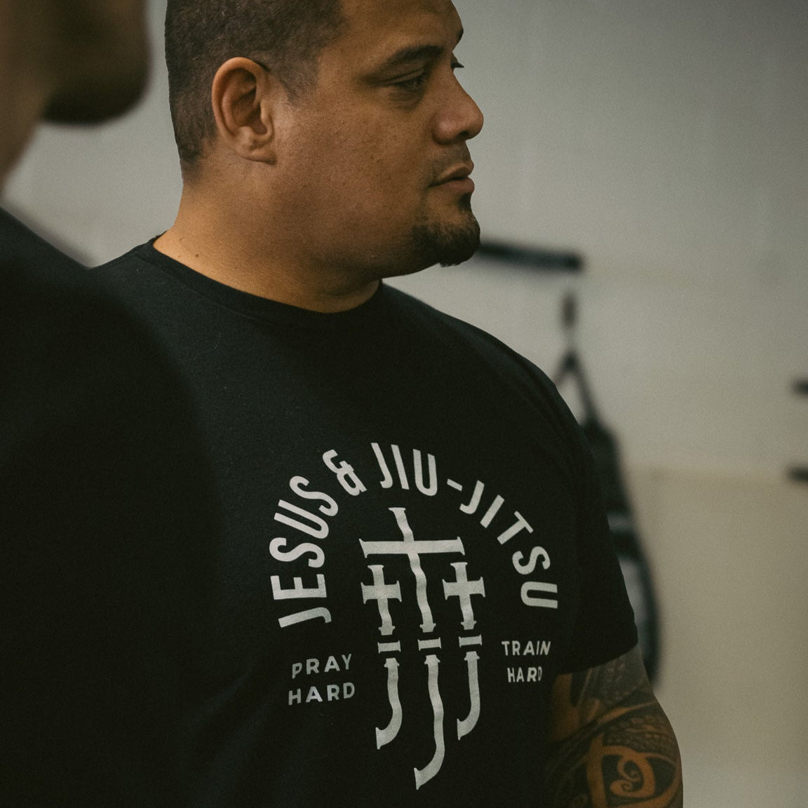 Man wearing a black t-shirt with white "JESUS & JIU-JITSU" text and logo on a gray background