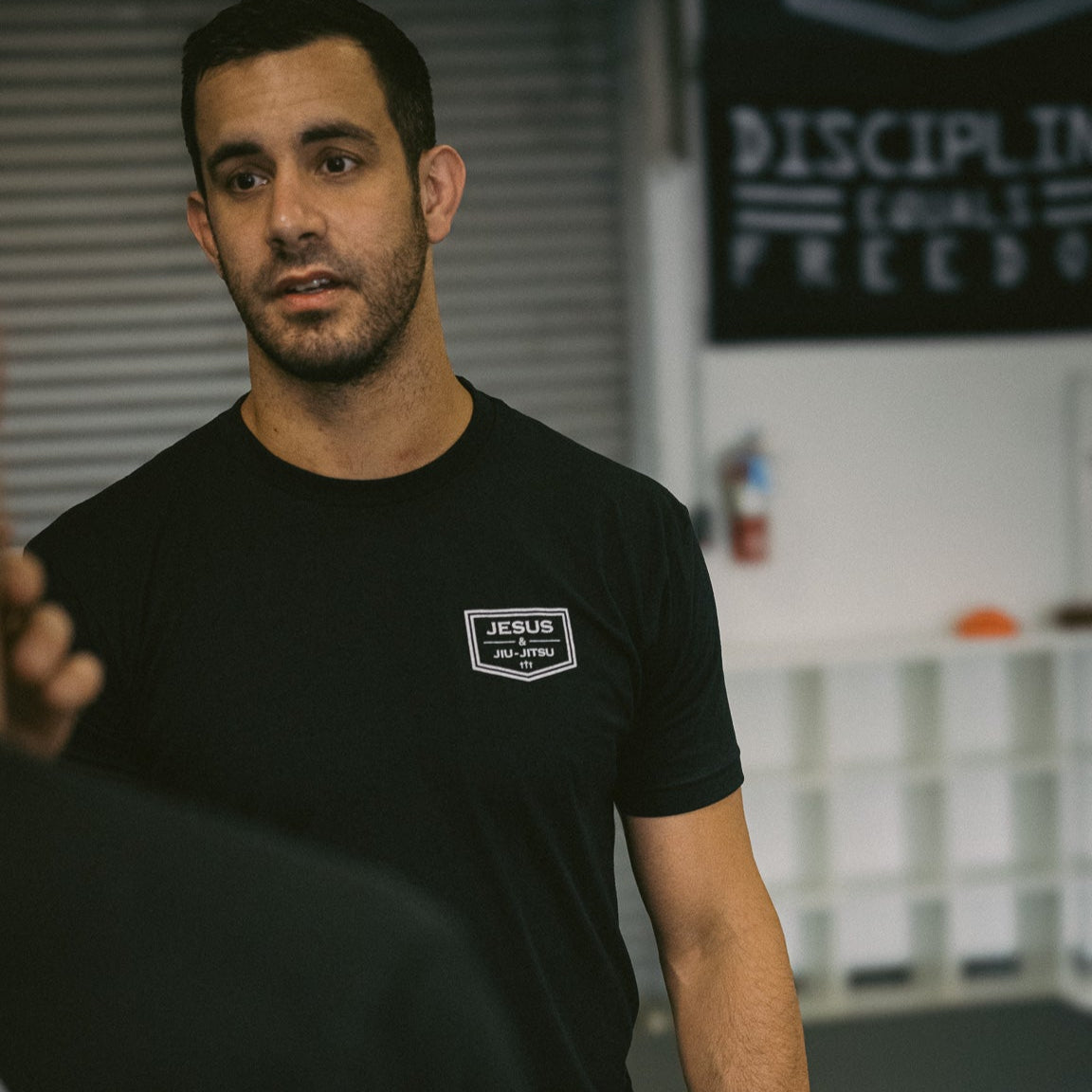 Man wearing a black t-shirt with a JJJ logo in an indoor setting