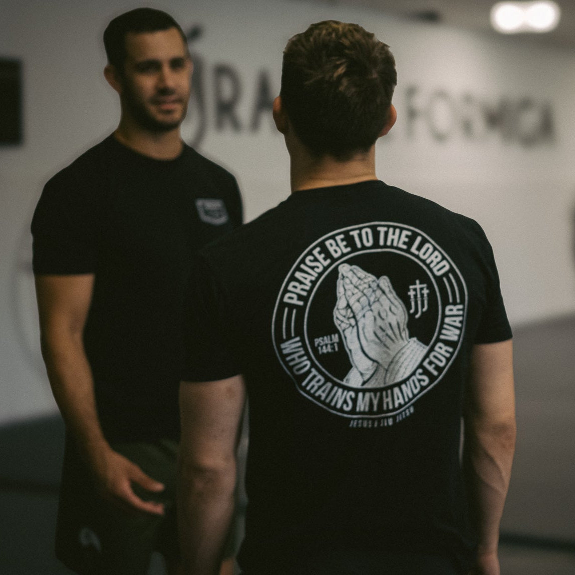 man wearing black tee with praying hands graphic on back with text "PRAISE BE TO THE LORD WHO TRAINS MY HANDS FOR WAR"